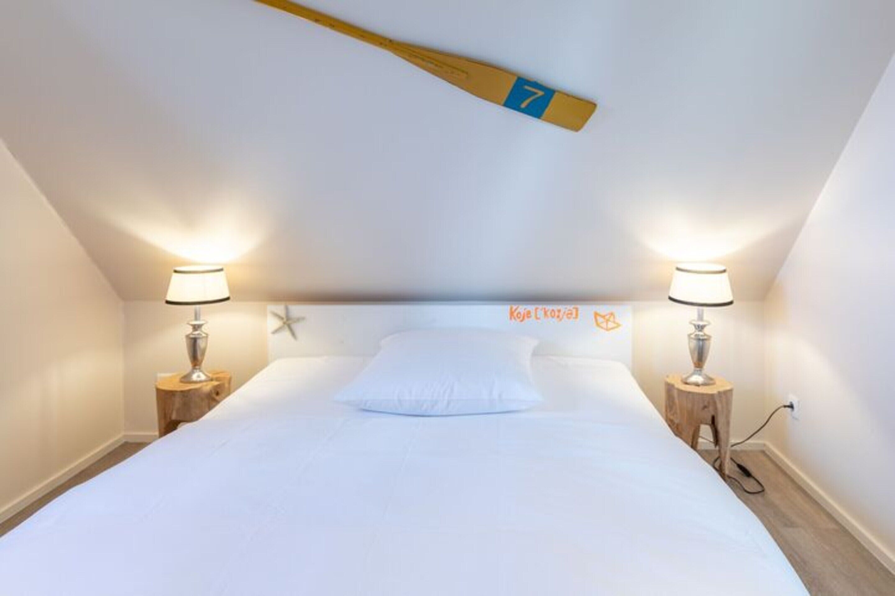 A bedroom with a bed, two bedside tables with lamps, a star decoration on the wall, and a wooden bat hanging from the ceiling.