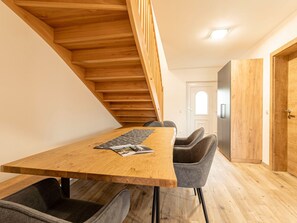 Un intérieur moderne avec une table à manger en bois, des chaises à revêtement gris, un escalier et une porte blanche.
