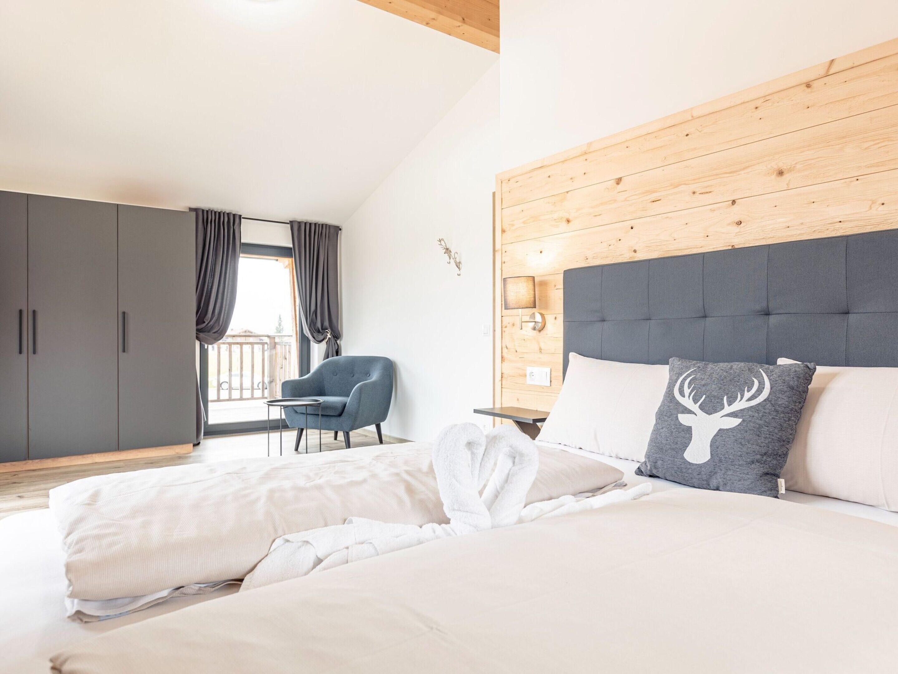 Un dormitorio con una cama grande, una silla, un armario y una ventana con cortinas.