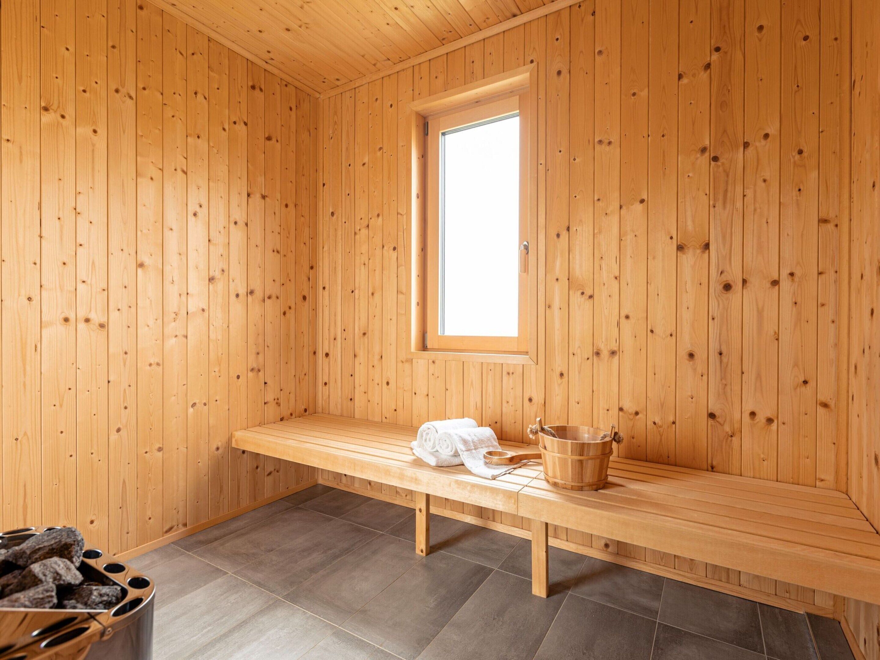 A wooden sauna room with a bench, a window, and a bucket.