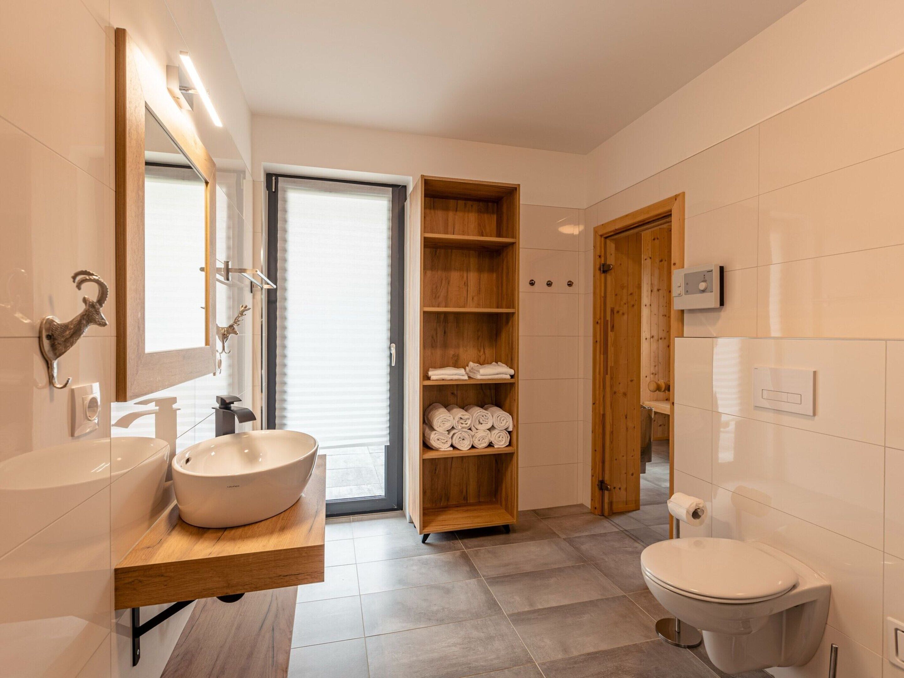 A modern bathroom with a large sink, a toilet, and a wooden shelf with towels.