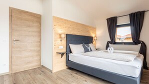 A bedroom with a wooden headboard, a bed with white bedding, a nightstand with a lamp, and a window with curtains. - Inzell Chalets With Private Pool (Inzell)
