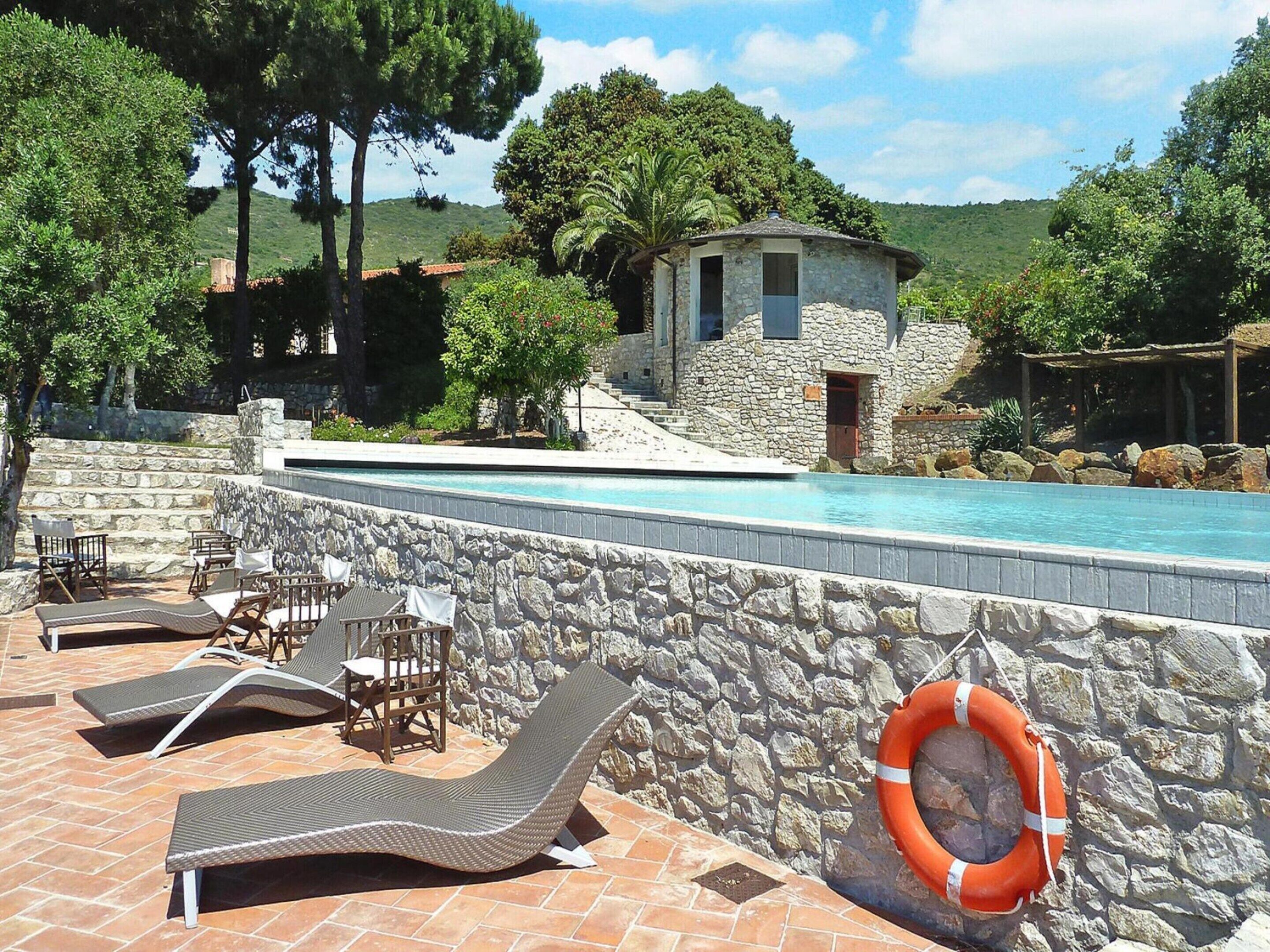 A pool area with stone walls, lounge chairs, and a small stone building.