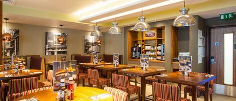 A restaurant with multiple dining tables and chairs, a counter with a menu, and overhead pendant lighting.