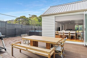 A wooden deck with a table and chairs, a fenced backyard, and a building with a sliding glass door. - Back Beach Portsea: 4  BR, 2.5  BA House in Portsea, Sleeps 7 (Portsea)