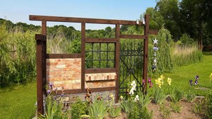 A garden with a wooden pergola, brick wall, and various plants including flowers and shrubs. - Ferienwohnung, Zemitz (Zemitz)
