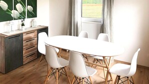 A dining area with a round table, white chairs, a wooden cabinet, and a window with curtains. - Ferienhaus am Partwitzer See, Elsterheide (Elsterheide)