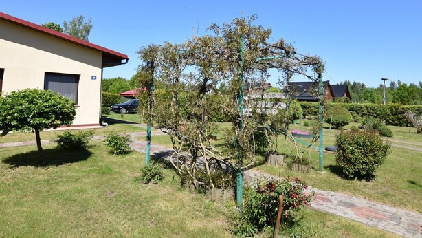 Een gebouw met een rood dak, een verharde oprit en een tuin met verschillende planten en een boom.