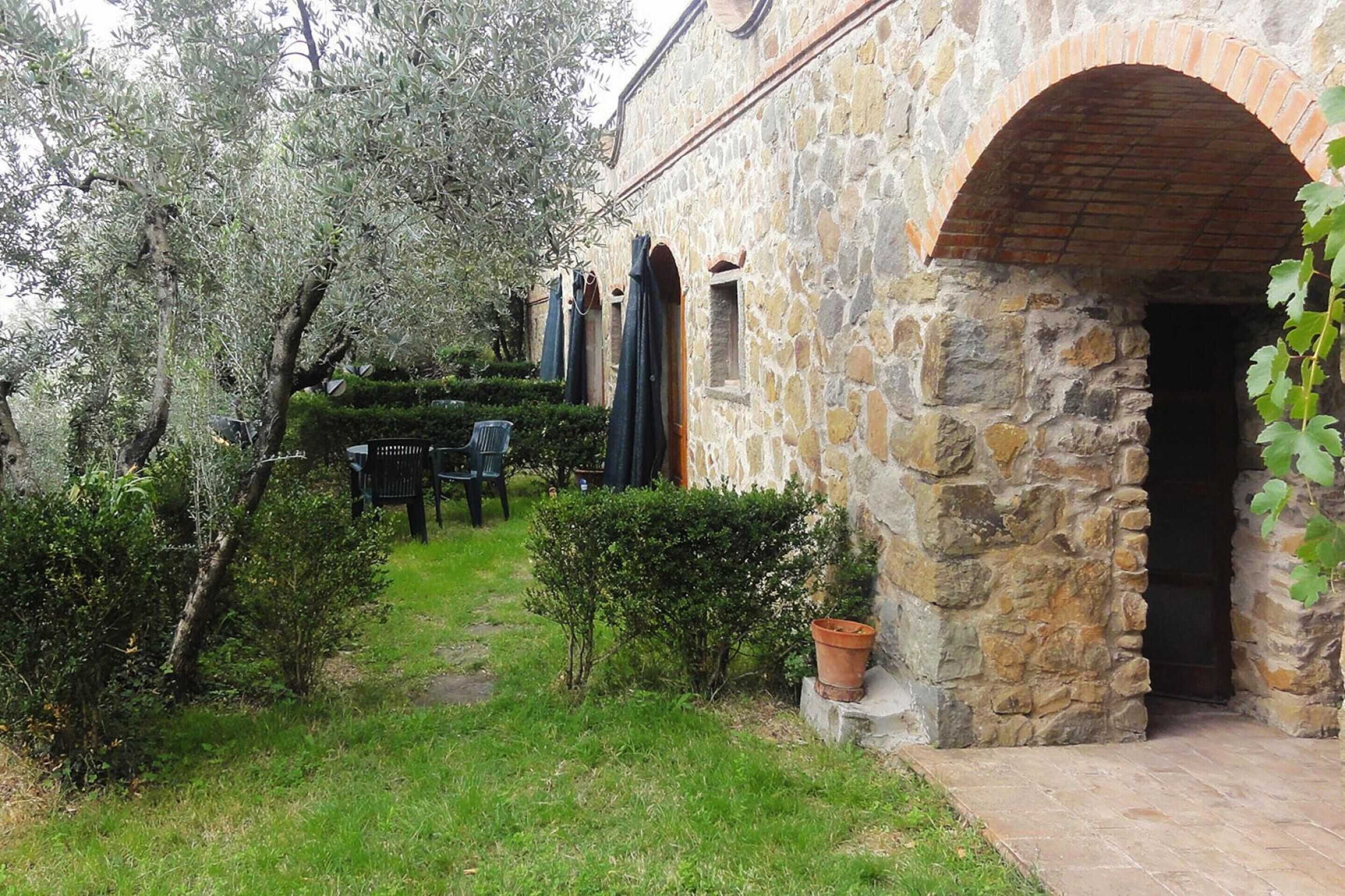 A stone building with an arched doorway, a small garden with a bench, and a potted plant.