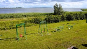 Zona verde con juegos infantiles, incluyendo columpios y un balancín, cerca de una masa de agua.
