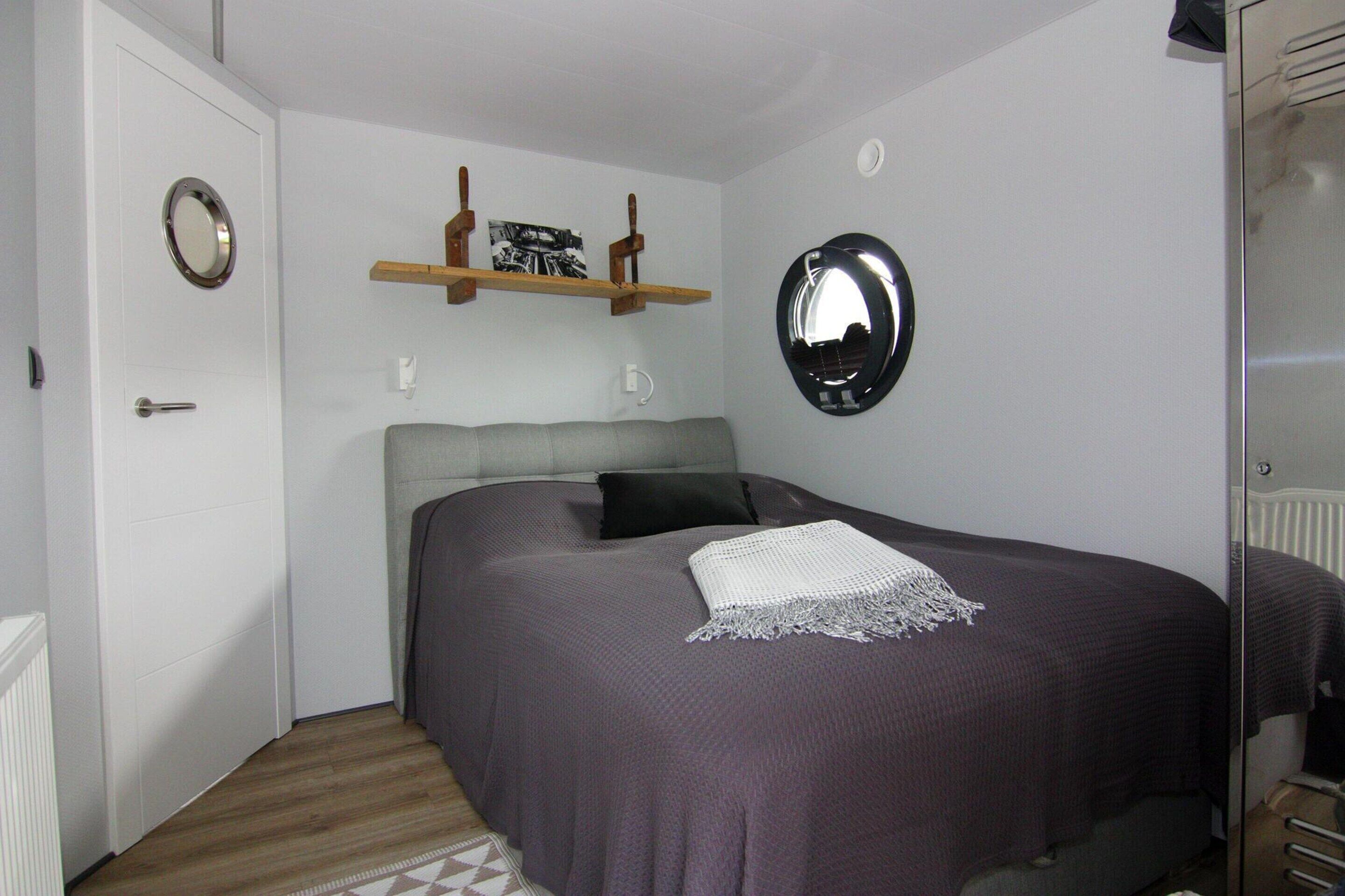 A bedroom with a bed, a mirror, a shelf with pictures, and a door.