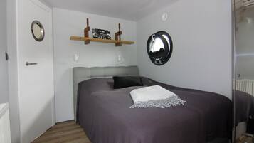 Ein Schlafzimmer mit Bett, Spiegel, einem Regal mit Bildern und einer Tür.
