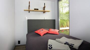 Ein modernes Schlafzimmer mit einem großen Bett, zwei roten Kissen und Blick auf Grünfläche.