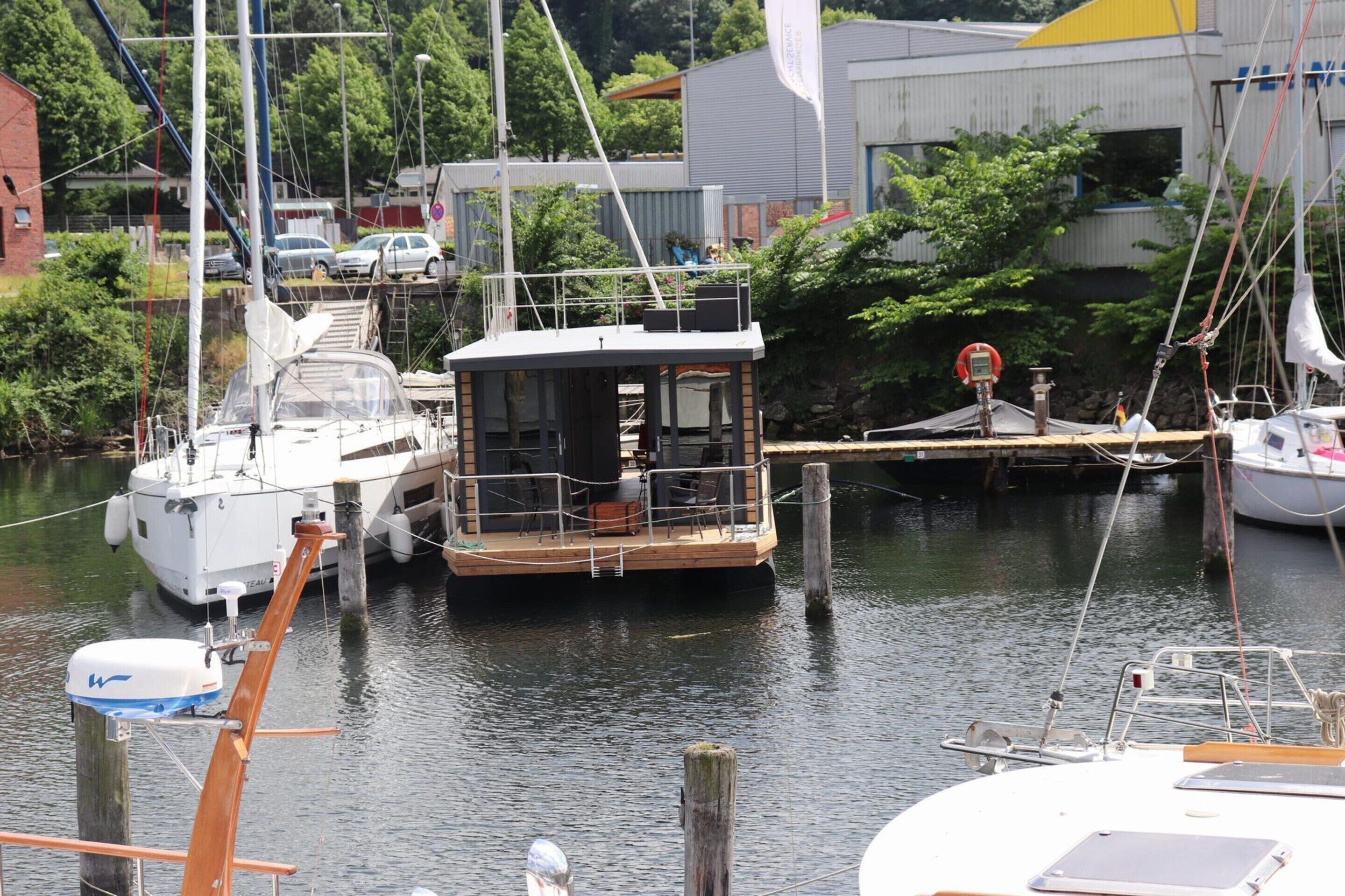 A marina with several boats docked, a small building with a deck, and a flagpole with a flag.