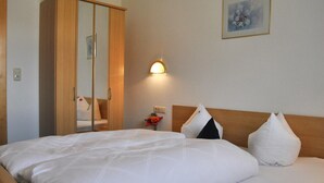 Hotellihuone, jossa on sänky, vaatekaappi, yöpöytä lampun kanssa ja seinällä oleva kehystetty kuva.