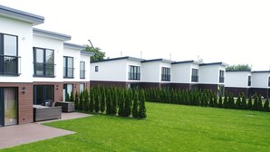 Un edificio residencial moderno con un césped cuidado y una fila de árboles de hoja perenne.