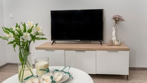A modern living room with a flat-screen TV on a wooden console table, a vase with flowers, a candle, and a plate with cookies. - Holiday Apartment Right on the Beach, Pobierowo (Rewal)