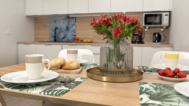 A modern kitchen with white cabinets, a microwave, and a vase with red flowers on the counter. - Holiday Apartment Right on the Beach, Pobierowo (Rewal)