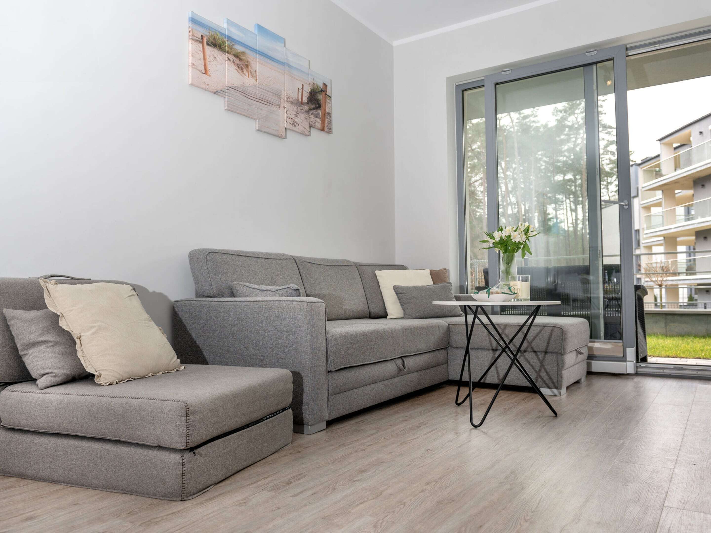 A modern living room with a grey sectional sofa, a small coffee table, and a large sliding glass door leading to an outdoor balcony.