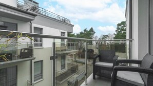 A balcony with glass railings, wicker furniture, and a view of the surrounding buildings. - Comfortable Holiday Apartment by the Beach (Rewal)