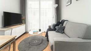 A modern living room with a grey sofa, a flat-screen TV, a round coffee table, and a large window with sheer curtains. - Comfortable Holiday Apartment by the Beach (Rewal)