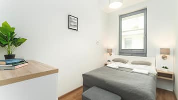 A modern bedroom with a bed, bedside tables, a window, a potted plant, and a small desk with books.