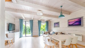En moderne stue med en hvid sofa, et spisebord med stole, et fjernsyn og et stort vindue med gardiner.
