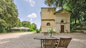 A rustic outdoor dining area with a table and chairs, a small building with a door and window, and a gravel path. - Apartment in Santo Pietro Belvedere With Pool-formerly TUI Ferienhaus (Capannoli)