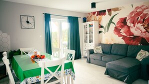 A dining area with a green table and white chairs, a gray sofa, and a cabinet with glass doors. - Holiday Home With Private Sauna, Jacuzzi and Pool (Koscierzyna)