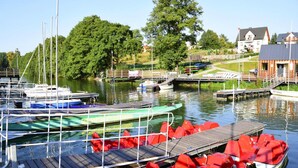 A marina with boats docked, a wooden pier, and a building in the background. - Holiday Home With Private Sauna, Jacuzzi and Pool (Koscierzyna)