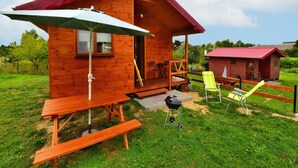 A wooden cabin with a porch, a picnic table, and a barbecue grill. - Cottages in a Quiet Neighborhood, Rusinowo (Postomino)