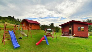 A playground with a slide and swings, two wooden cabins with red roofs, and a grassy area. - Cottages in a Quiet Neighborhood, Rusinowo (Postomino)