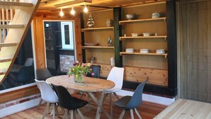 Ein gemütliches Holzinnere mit einem runden Holztisch, umgeben von Stühlen, einer Treppe und Regalen mit dekorativen Gegenständen.