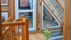 Eine Holztreppe führt zu einem Erker mit Glasdach, einer Ziegelwand und Blick auf einen Balkon.