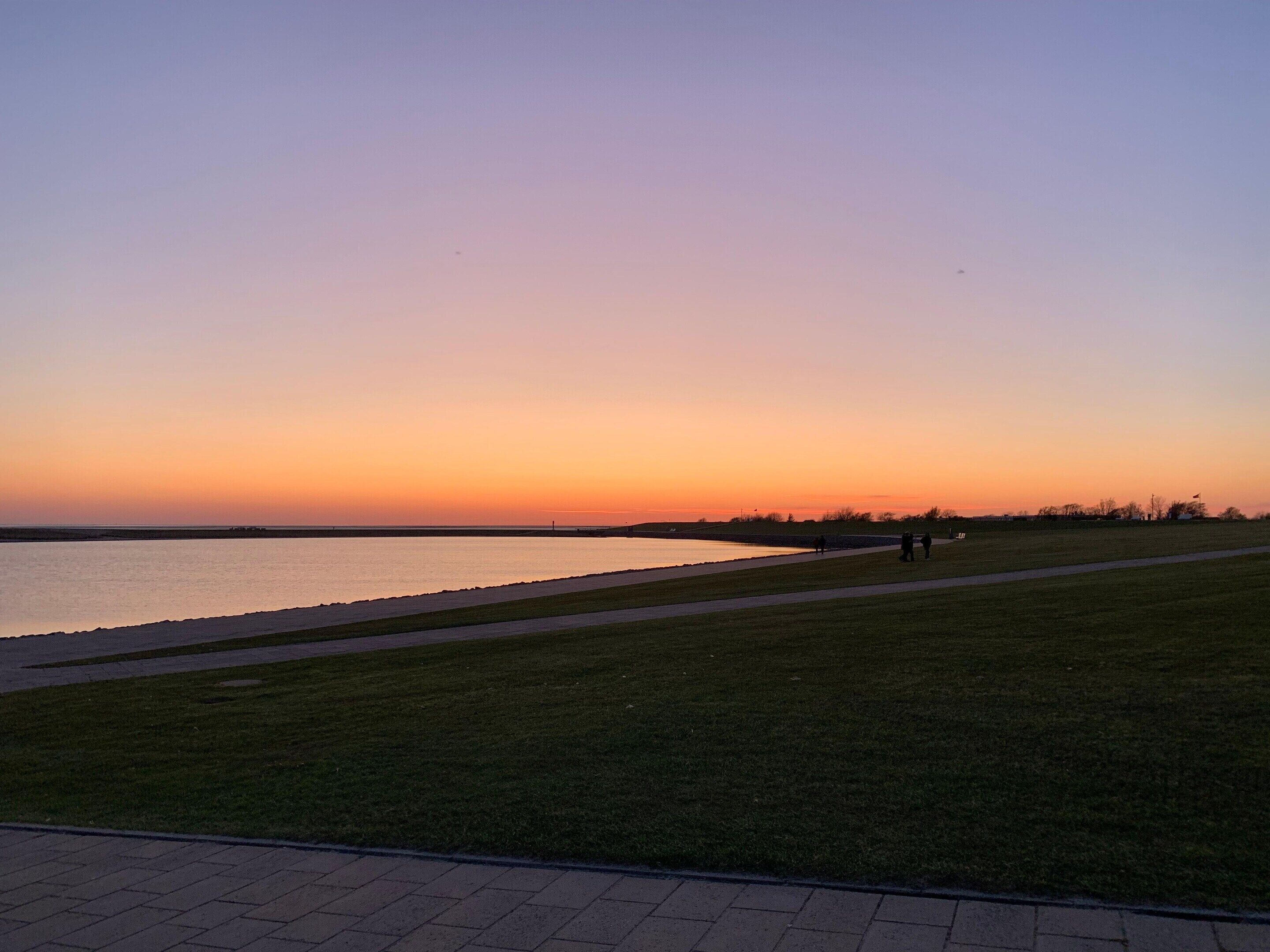 A grassy area with a paved path beside a body of water during sunset.