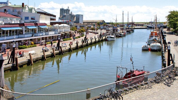 Un puerto deportivo con barcos amarrados, un hotel de techo rojo y un paseo peatonal junto al agua.
