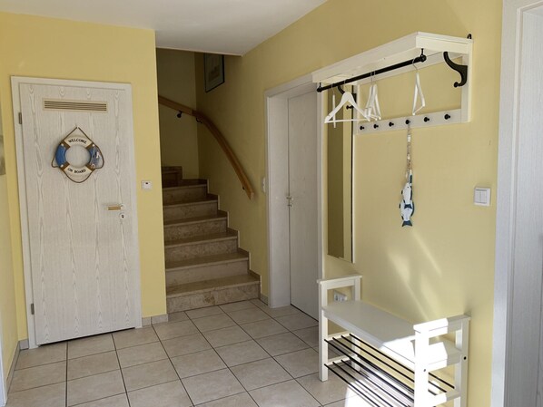 A hallway with a wooden door, a staircase, and a white bench with a metal rack. - Ferienhaus Marlina Glueckstreffer in Busum Nahe (Büsum)