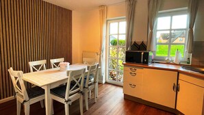 Una cocina compacta con comedor, piso de madera y vista al exterior a través de un ventanal grande.