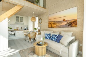 A modern kitchen with white cabinets, a dining area with a wooden table and chairs, and a living room with a beige sofa and a painting of a beach scene. - House With a Terrace, Whirlpool, Wrzosowo (Kamien Pomorski)