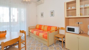 A compact living space with a sofa, dining table, chairs, a microwave, and a cabinet. - Apartments Cormoran, Bibione Lido del Sole (San Michele al Tagliamento)