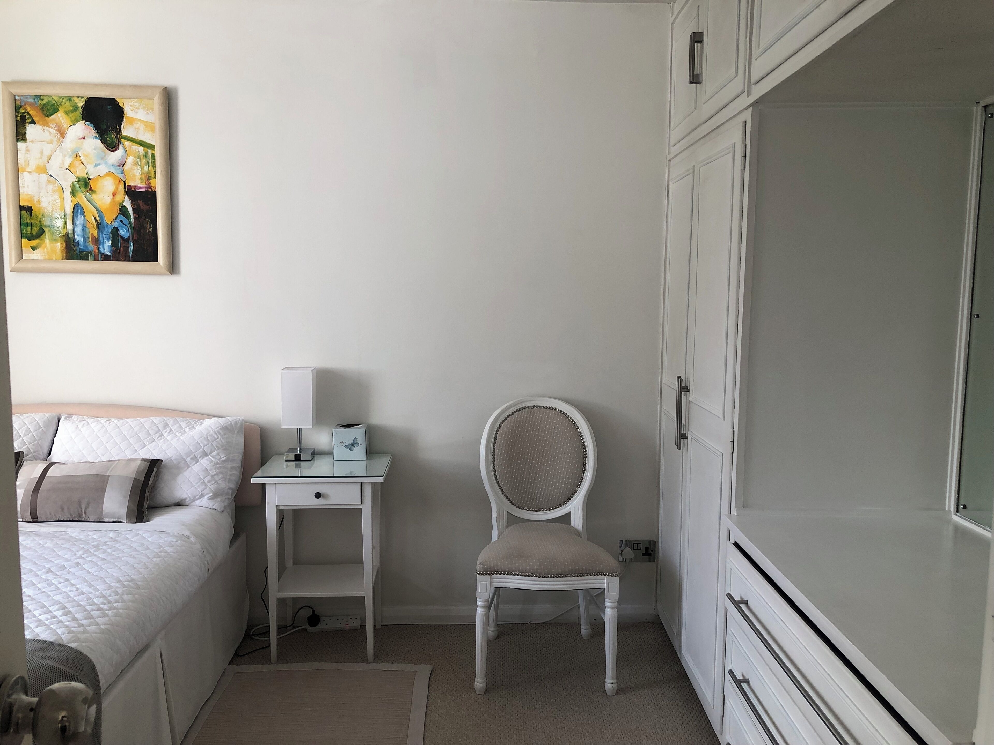A bedroom with a bed, a bedside table with a lamp, a chair, and a wardrobe.