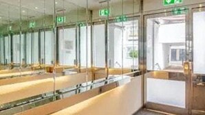 A modern hotel lobby with a long reception desk, glass partitions, and an exit door with a green sign.