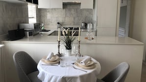 A modern kitchen with white cabinets, a dining area with a table set for two, and a small island with a candle and decorative items.