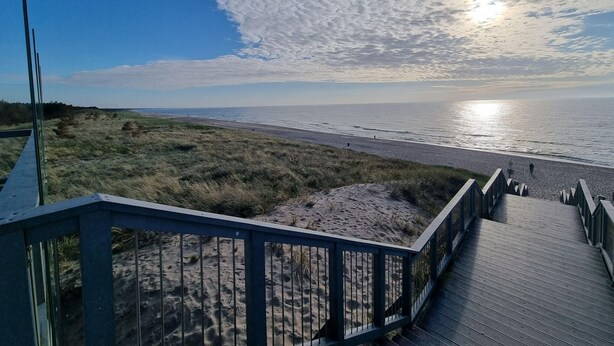 A wooden boardwalk leading to a beach with dunes and a clear sky. - Unique Apartment With a Balcony in Darlowko (Darlowo)