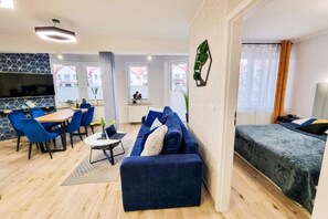 Ein modernes Wohnzimmer mit Sofa, Esstisch, Stühlen, Fernseher und einem Bett mit Blick aus dem Fenster.