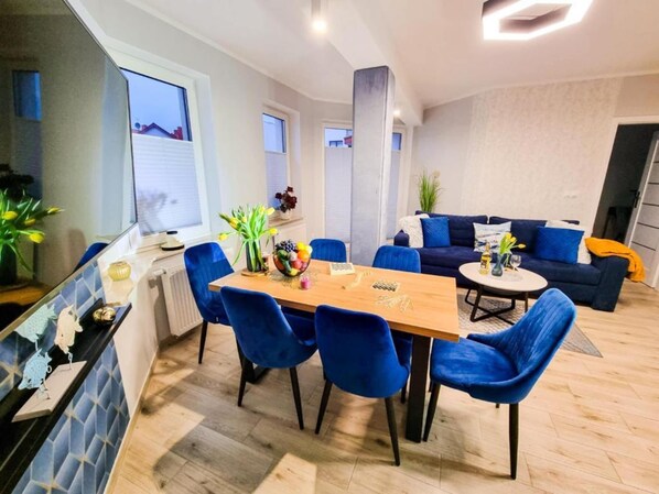 Ein modernes Wohnzimmer mit Essbereich, bestehend aus blauen Stühlen, einem Holztisch und einem dunkelblauen Sofa.
