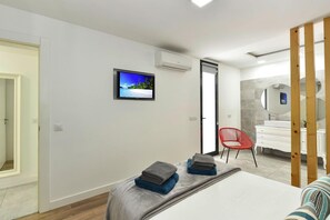 A modern bedroom with a bed, a TV, a red chair, and a bathroom visible through an open door. - Bungalow, Playa del Ingles (San Bartolomé de Tirajana)