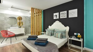 A modern bedroom with a large bed, a bedside table, a red chair, and a bathroom with a mirror and sink. - Bungalow, Playa del Ingles (San Bartolomé de Tirajana)