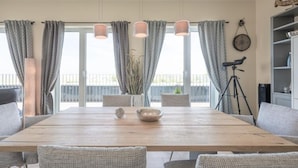 A dining area with a wooden table, grey upholstered chairs, and a potted plant. - Appartement in Fantastischer Lage auf Nordstrand (Nordstrand)