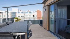 A balcony with a table and chairs, a sliding glass door, and a view of neighboring buildings. - Appartement in Fantastischer Lage auf Nordstrand (Nordstrand)